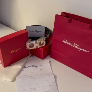 Svart skärp från Salvatore Ferragamo - Snyggt svart skärp från Salvatore Ferragamo med ikoniskt silverfärgat spänne. Kommer med originalförpackning, dustbag och kvitto. Perfekt accessoar för att lyfta din outfit med en exklusiv touch.