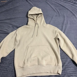 Beige hoodie med huva och magficka - Snygg beige hoodie med klassisk huva och dragsnören. Hoodien har en stor magficka framtill och ribbade muddar vid ärmslut och nederkant. Perfekt för en avslappnad och stilren look.
