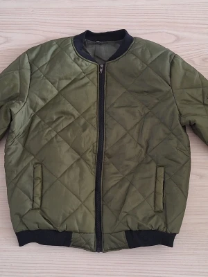 Olivgrön quiltad pufferjacka stl L - Snygg olivgrön pufferjacka med quiltat mönster och svarta ribbade muddar vid ärmslut och nederkant. Jackan har dragkedja framtill och två fickor på sidorna. Perfekt för kalla dagar och ger en trendig look. Köpt från fruugo för 479 kr. För dyrt att returnera, säljer därför. 
