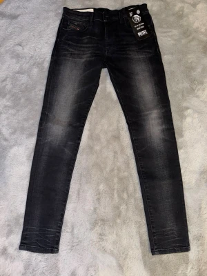 Svarta skinny jeans från Diesel - Snygga svarta skinny jeans från Diesel med diskret slitning och klassisk femficksdesign. Jeansen har en smal passform och cool tvättad look, perfekt för en trendig streetstyle. Märkesdetaljer syns på fickan och bak. Materialet är stretchigt denim för extra komfort. Helt nya 31/32