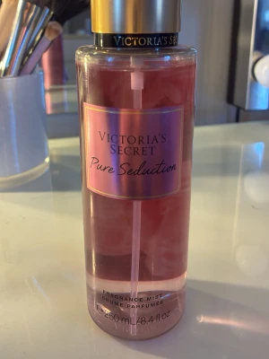 Victoria's Secret Pure Seduction mist - En rosa parfymmist från Victoria's Secret med doft av plommon och fresia. Flaskan är genomskinlig med guldigt lock och rymmer 250 ml. Perfekt för dig som gillar fruktiga och blommiga dofter. Använd enstaka gånger så flaskan är i princip full