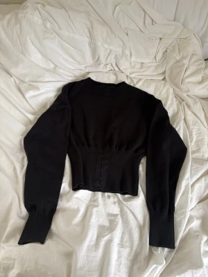 Svart stickad cropped tröja - Säljer en svart stickad tröja med cropped passform och långa ärmar. Tröjan har en tight midja och breda muddar vid ärmslut. Perfekt för dig som gillar en stilren och trendig look. Materialet är mjukt och stretchigt.