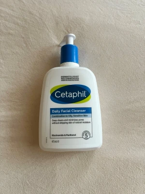 Cetaphil Daily Facial Cleanser 473 ml - Cetaphil Daily Facial Cleanser för kombinerad till oljig och känslig hud. Djup rengöring som minimerar porer utan att torka ut huden. Innehåller niacinamid och panthenol. Kommer i en vit plastflaska med blå pump och etikett. Helt ny, inte använd.