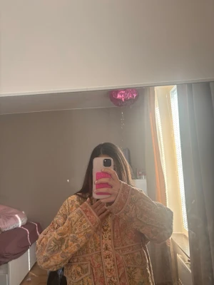 Mönstrad quiltad jacka i pastell - Unik quiltad jacka med blommigt mönster i pastellfärger som rosa, gult och grönt. Jackan har breda ärmar, synliga sömmar och dekorativa kanter. Perfekt för dig som gillar boho-stil och vill sticka ut med en färgglad och mysig look.