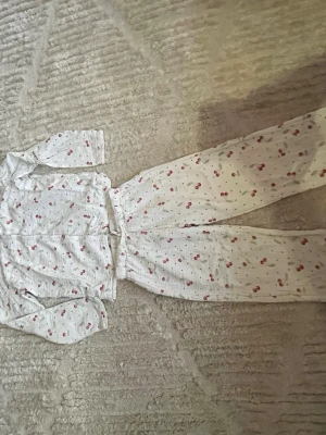 Vit pyjamas med körsbärsmönster - Supermysig vit pyjamas med långärmad skjorta och byxor, dekorerad med söta små körsbär över hela setet. Perfekt för chillkvällar hemma. Mjukt och lätt material som känns skönt mot huden.
