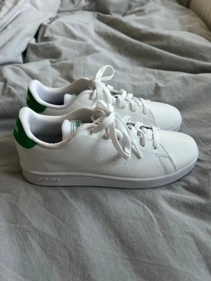 Vita Adidas sneakers med gröna detaljer - Snygga vita sneakers från Adidas med klassisk designe och gröna detaljer på hälen. Helt nya men utan prislapp. Storlek 38 och 2/3