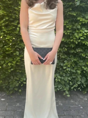 Lång ljusgul sidenklänning - Elegant långklänning i ljusgult  med draperad överdel och smal passform. Klänningen har en axelbandslös design och faller snyggt längs kroppen. Perfekt för bal. Som man ser på bilden enstaka fläckar längst ner på klänningen (syns inte tydligt)