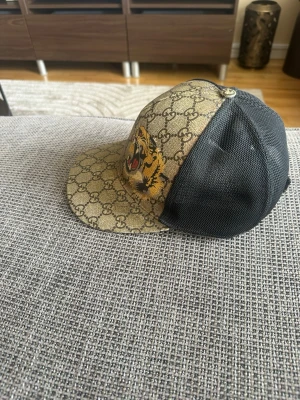 Gucci keps med tiger och GG-mönster - Hej, jag säljer min Gucci-keps som inte längre kommer till användning. Kepsen är i bra skick, men framtill är den lite kladdig – inte mycket, utan bara lite. Tyvärr har jag inget kvitto kvar, men den är 100 % äkta. Jag köpte den sommaren 2021 för 2800 kr. 