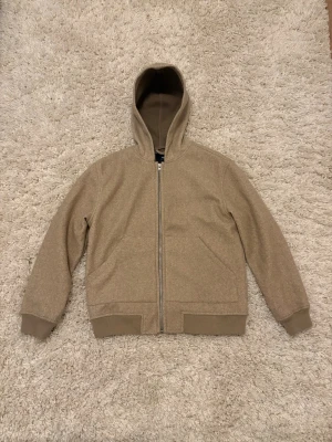 Beige hoodie från Pull&Bear - Snygg beige hoodie från Pull&Bear med dragkedja framtill och ribbade muddar vid ärmslut och nederkant. Tillverkad i ett mjukt material, för dig som gillar en clean och enkel stil. 