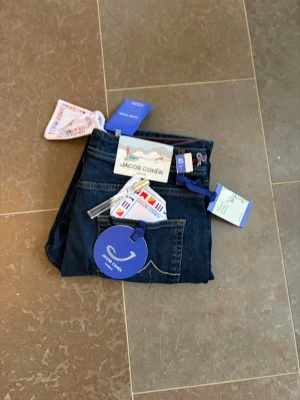 Mörkblå jeans från Jacob Cohën - Säljer ett par mörkblå jeans från Jacob Cohën med klassisk femficksmodell och snygga kontrastsömmar. Jeansen har en broderad J-logga på fickan och detaljerade innerfoder. Perfekta för dig som gillar premiumkänsla och stilren design. Pris diskuterbart😉