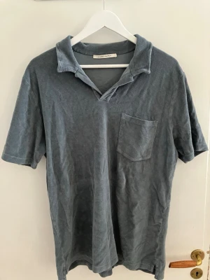 Blå t-shirt med krage och ficka - Snygg blå t-shirt från Saturdays NYC med avslappnad krage och bröstficka. T-shirten har korta ärmar och en loose passform, perfekt för en chill och stilren look. Tillverkad i mjuk bomull för extra komfort.