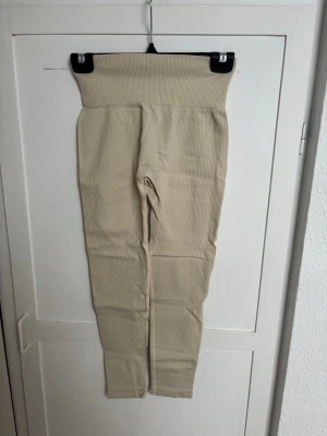 Beige ribbade leggings med hög midja - Snygga beige leggings med ribbad struktur och extra hög midja. Stretchigt material som sitter skönt och formar sig efter kroppen. Perfekta för en avslappnad och trendig look. Inga synliga fickor eller detaljer, minimalistisk design.