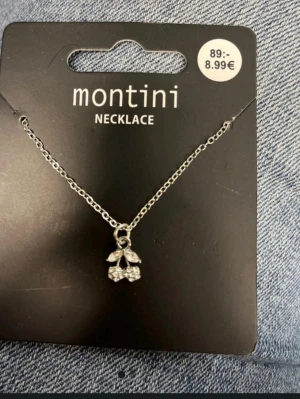 Silverfärgat halsband med körsbär Montini - Snyggt silverfärgat halsband från Montini med ett hängsmycke i form av körsbär dekorerat med små glittrande stenar. Kedjan är tunn och smidig, perfekt för att ge en söt touch till din outfit. Passar dig som gillar detaljer och stilrena accessoarer.