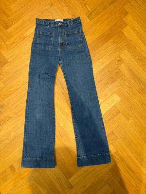 Blå utsvängda jeans med fickor - Snygga blå jeans med utsvängda ben och stora fickor fram och bak. Jeansen har hög midja och klassisk denimlook, perfekta för en avslappnad stil. Materialet är denim i bomull. Passar dig som gillar retrovibbar och bekväma jeans. Modell SW006, Vintage 95