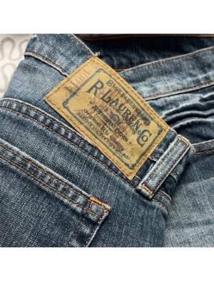 Blå jeans från Ralph Lauren Sport - Säljer ett par klassiska blå jeans från Ralph Lauren Sport med snygga kontrastsömmar och vintage-inspirerad patch på bakfickan. Jeansen är tillverkade i 99% bomull och 1% elastan för en bekväm passform. Perfekt för dig som gillar tidlös stil. Ej använd.
