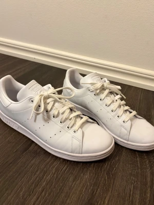 HERR Vita Adidas Stan Smith sneakers - Klassiska helvita Adidas Stan Smith sneakers i lågt snitt. Skorna har en stilren design med perforerade ränder på sidorna, vita skosnören och diskret Adidas-logga på plösen och hälen. Använda 1 gång så i nyskick! Nypris ca 1400kr. Storlek 44. 