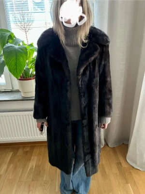 Mörkbrun vintage äkta mink päls-kappa - Säljer en lång, mörkbrun päls-kappa i klassisk mink vintage-stil. Kappan har bred krage och rak passform, perfekt för dig som vill ha en tidlös och lyxig look. Pälsen ger en mjuk och varm känsla, och kappan stängs framtill med dolda knappar.
