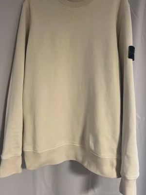 Beige sweatshirt från Stone Island - Snygg beige/halvgul sweatshirt från Stone Island med klassisk rund hals och ikonisk logotyp-patch på vänster ärm. Tröjan har en avslappnad passform och är tillverkad i mjukt bomullsmaterial. Perfekt för en stilren och trendig look. Köpt på NK sommaren 2024 men knappt använd då den var lite stor för mig, kan förmodligen hitta kvitto om de är av intresse. Även priset går väl att sänka om affären är smidig