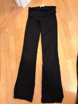 Gina yoga pants tall  - Säljer ett par svarta leggings med bootcut-ben och bred linning som kan vikas ner. Sköna och stretchiga, perfekta för en avslappnad look. Materialet känns mjukt och följsamt, troligen bomullsmix eller liknande. Passar dig som gillar enkel och stilren design.