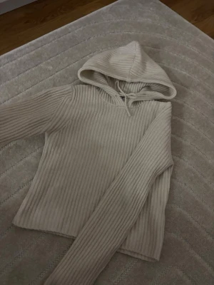 Beige ribbad hoodie från Stradivarius - Säljer en beige ribbad hoodie från Stradivarius med huva och dragsko. Tröjan har långa ärmar och är tillverkad i ett mjukt, stickat material som känns riktigt skönt mot huden. Perfekt för dig som gillar en enkel men snygg stil.