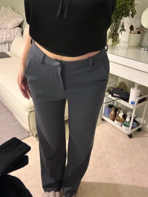 Mörkgrå/ blåa kostymbyxor med raka ben - Snygga mörkgrå kostymbyxor med raka ben och klassisk passform. Byxorna har hällor för skärp och diskreta fickor fram. Perfekta för en stilren och modern look. Materialet känns mjukt och följsamt.