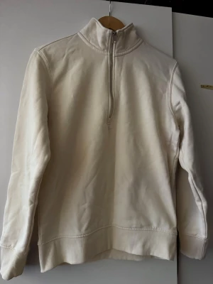 Vit halvzip hoodie med hög krage - Säljer en stilren vit hoodie med halvzip och hög krage. Tröjan har ribbade muddar och är tillverkad i mjukt material som passar perfekt för en avslappnad look. Ingen huva, enkel och clean design.