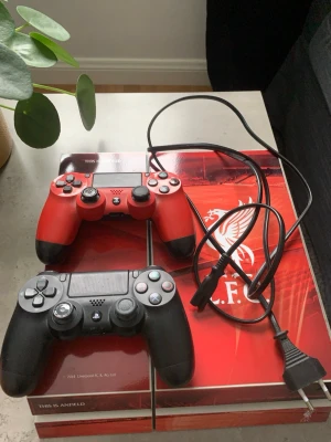 PlayStation 4 Liverpool Edition + 2 kontroller - Säljer en PlayStation 4 med unik Liverpool FC design. Konsolen är röd med vita detaljer och har klubbens logga. Två trådlösa DualShock 4-kontroller ingår, en röd och en svart. Strömkabel medföljer. Perfekt för gaming och fotbollsfans!