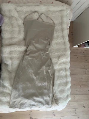 Beige satin klänning med öppen rygg  - Beige satin klänning med öppen rygg  Defekter finns se på bild 4 Perfekt för sommaren man kan byta ut smörerna på ryggen till egna.   