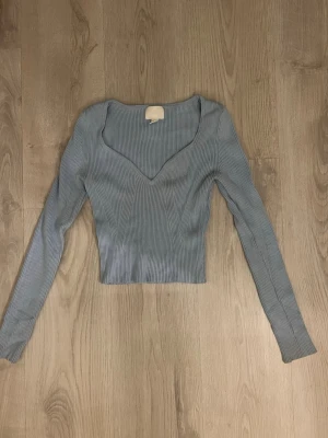 Ljusblå ribbad topp från H&M - Trendig ljusblå ribbad topp från H&M med lång ärm och snygg v-ringning. Croppad modell i storlek xs. 