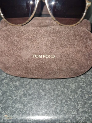 Tom Ford solglasögon pilotmodell med kvittot  - Snygga solglasögon från Tom Ford i klassisk pilotmodell. Bågarna är i en metallfärg med mörka linser och kommer med ett brunt fodral i mocka-look med Tom Ford-logga. Tillverkade i Italien och ger en exklusiv känsla till din stil.