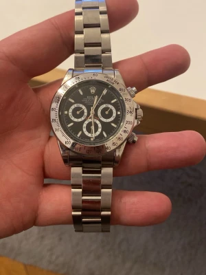  silver herrklocka automatiskt  - Snygg  Daytona herrklocka i rostfritt stål med svart urtavla och silverfärgade detaljer. Klockan har kronograf-funktion och klassisk länkarmband i metall. Perfekt för dig som gillar exklusiva accessoarer med sportig känsla.