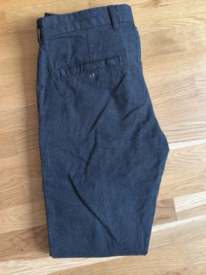 Mörkgrå kostymbyxor East West - Snygga mörkgrå kostymbyxor från East West med klassisk passform. Byxorna har bälteshällor, knappgylf och en bakficka med knapp. Perfekta för en clean och stilren look.