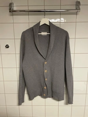 Grå cardigan  - Snygg grå kofta/cardigan med fem knappar framtill. Koftan har långa ärmar och är tillverkad i ett mjukt stickat material. Perfekt för lager-på-lager och enkel att matcha med olika outfits.