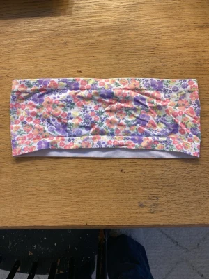 Blommig bandeau bikiniöverdel New Look - Söt bandeau bikiniöverdel från New Look med blommigt mönster i lila, rosa, orange och vitt. Tunn och stretchig modell som sitter bekvämt över bysten. Perfekt för dig som gillar färgglada och somriga badkläder.