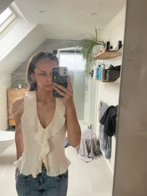 Vit omlott linnetopp med volang - Säljer en vit omlott linnetopp med volangdetaljer och v-ringning från Nelly. Toppen är ärmlös och har en vågig struktur i materialet. Knappt använd och kan även passa personer som har XS💕💕