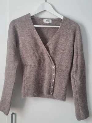 Omlottkofta med knappar Gina Tricot  - Detta är en beige/brun stickad kofta med v-ringning och knappar,  från Gina Tricot.