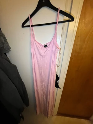 Ljusrosa långklänning med smala band - Säljer en enkel och stilren ljusrosa långklänning med smala axelband och v-ringning. Klänningen har en rak passform och är tillverkad i ett mjukt, tunt material som känns skönt mot huden. Perfekt för varma dagar eller sommarens alla tillfällen.