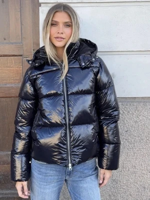 Svart glansig pufferjacka från Nelly  - Säljer en svart, glansig pufferjacka med stor huva och dragkedja framtill. Jackan har breda kanaler och en boxig passform som ger en cool look. Perfekt för kalla dagar när du vill hålla dig varm och samtidigt se trendig ut.