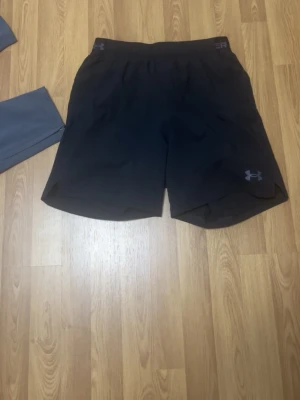 Svarta träningsshorts från Under Armour - Snygga svarta träningsshorts från Under Armour med elastisk midja och diskret logga på benet. Perfekta för gymmet eller löprundan, tillverkade i lätt och snabbtorkande material för maximal komfort.