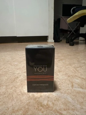 Emporio Armani Stronger With You - Emporio Armani Stronger With You Absolutely är en parfym i en elegant svart och kopparfärgad kartong. Flaskan är troligtvis av glas och förpackningen har en modern, stilren design med metalliska detaljer. Doften är känd för sin intensiva och maskulina karaktär.