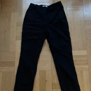 Svarta kostymbyxor med raka ben - Svarta kostymbyxor med klassisk rak passform. Byxorna har hällor för bälte och är tillverkade i ett slätt material som ger en stilren look. Säljer eftersom de är för korta på mig, nästan aldrig använt. Katt finns i hemmet. 