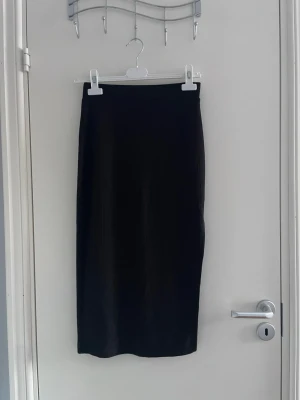 Svart ribbad långkjol - Säljer en svart ribbad långkjol med tight passform. Kjolen har en enkel och stilren design som passar perfekt till många olika outfits. Materialet är stretchigt och följsamt för en bekväm känsla.