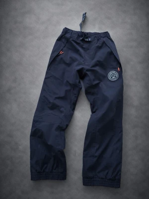 Mörkblå täckbyxor Dope - Säljer ett par mörkblå täckbyxor från Dope med resår i midjan och benslut. Byxorna har två fickor med dragkedja och en snygg logga på ena benet. Perfekta för kalla dagar och outdoor-aktiviteter.