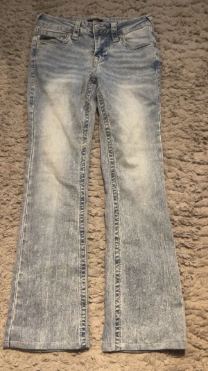Ljusblå bootcut jeans från true religion - Säljer ett par ljusblå bootcut jeans från True religion med slitna detaljer och klassisk soaped tvätt. Jeansen har fem fickor, bälteshällor och knappar på bakfickorna. Materialet är denim i bomull och passformen är något utsvängd nedtill. Jeansen är uppsydda några centimeter!! De är aldrig använda utomhus bara provade