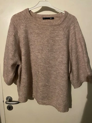 Beige stickad tröja med halvlånga ärmar - Mysig beige stickad tröja med vida ärmar. Tröjan har en avslappnad passform och är tillverkad i ett mjukt material. Enkel och stilren design som funkar till det mesta.