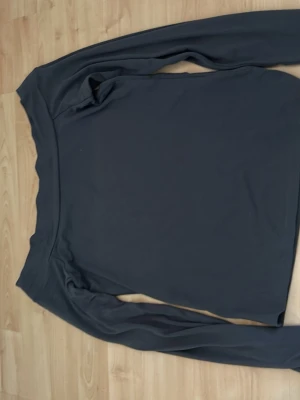 Mörkgrå långärmad offshoulder topp - Snygg mörkgrå långärmad topp med offshoulder-design. Toppens material känns mjukt och stretchigt, perfekt för en stilren look. Passformen är slim och toppen är enfärgad utan mönster eller detaljer.