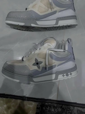 Lv skates  - Snygga sneakers från Louis Vuitton i grått och vitt med meshpaneler och detaljer i läder. Skorna har LV-logga på plösen och sidorna samt en unik sula med grafiska symboler. Perfekta för dig som gillar exklusiv streetwear och vill sticka ut.