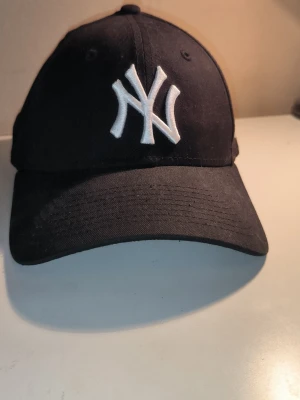 Svart New Era Yankees keps - Säljer en svart keps från New Era med klassiskt New York Yankees-broderi i vitt framtill och New Era-logga på sidan. Kepsen har böjd skärm och är tillverkad i bomullstyg. Perfekt för dig som vill ha en stilren och clean keps som funkar till allt. Priset är ej hugget i sten!