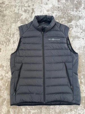 Svart dunväst från Sail Racing - Svart dunväst från Sail Racing. Västen har hög krage, två dragkedjeförsedda fickor och quiltad design. Mycket fint skick! 