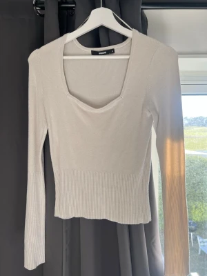 Vit ribbad topp från Bik Bok - Trendig vit topp från Bik Bok med ribbade detaljer och lång ärm. Toppen har en djup, fyrkantig ringning framtill och är tillverkad i ett stretchigt material som sitter snyggt på kroppen. Perfekt att styla med jeans eller kjol.